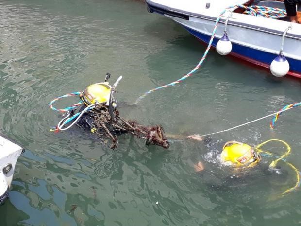 Two Venice canal divers in yellow helmets surfacing with debris retrieved from a harbor waterway