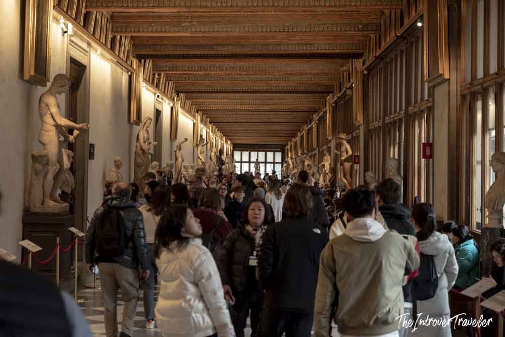Crowded main corridor of the Uffizi Gallery Florence, lined with classical sculptures and gilded ceilings