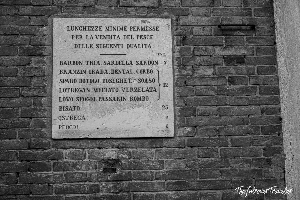 Stone plaque at Venice Rialto fish market listing minimum legal sizes for selling local fish species