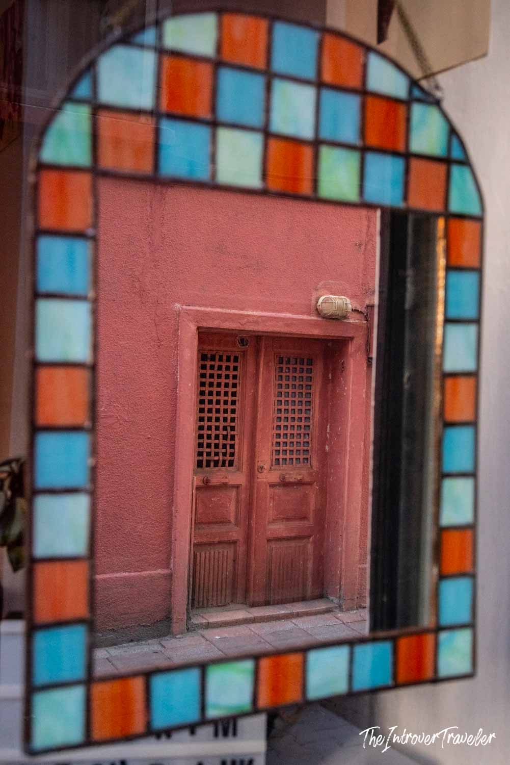 Colorful stained glass mirror reflecting a rustic pink door and facade in Kadıköy, Istanbul