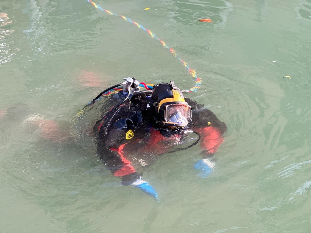 Scuba diver in full gear surfacing in a Venice canal, tethered by a colorful safety rope