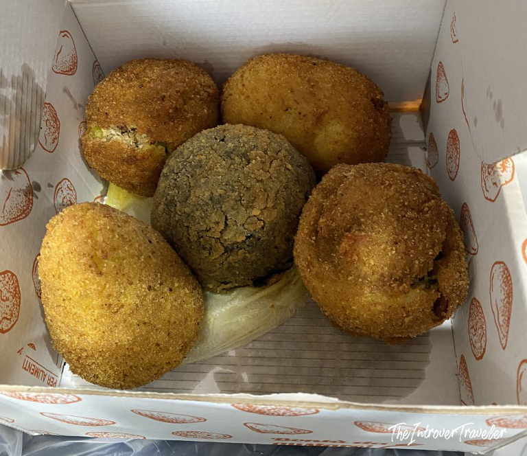 Five golden fried arancini in a takeaway box, a classic Sicilian street food snack in Favignana