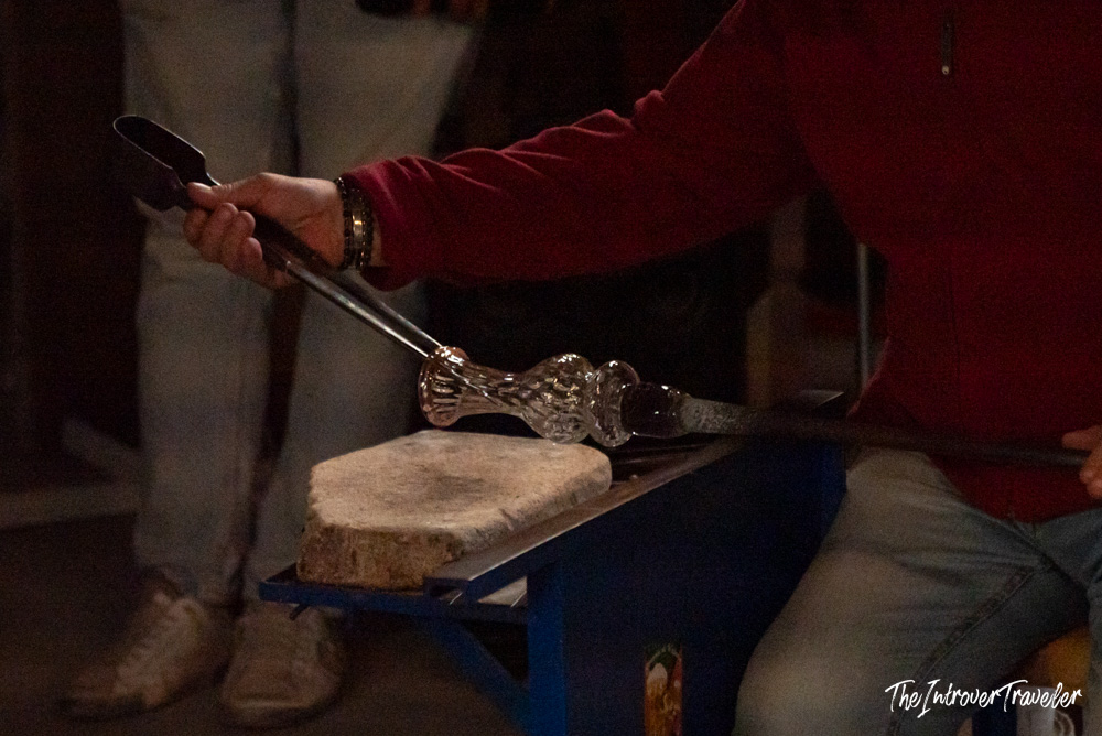 Murano glassblower shaping a molten glass vase with metal tongs on a wooden rest