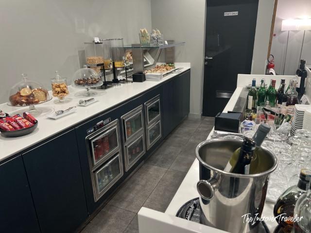 Piranesi Lounge Linate buffet counter with snacks, pastries, wine bucket, and refrigerated drinks