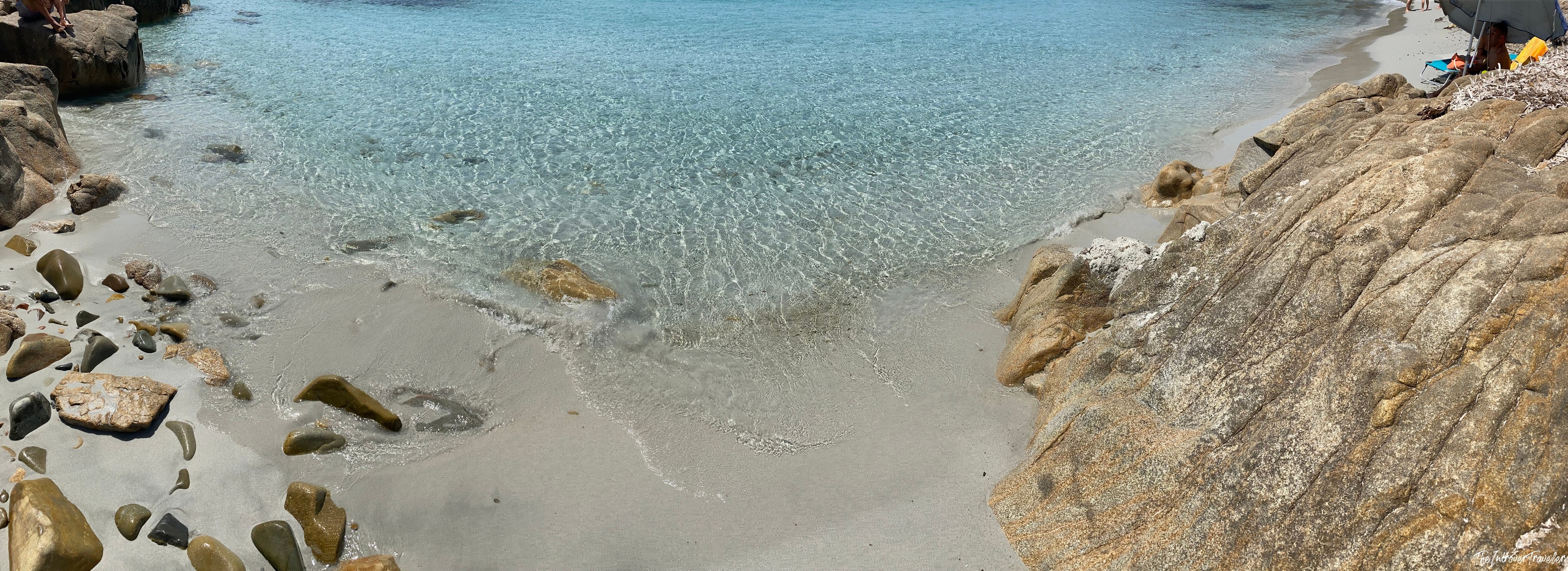Crystal clear turquoise water lapping white sand between granite rocks at a south Sardinia beach cove