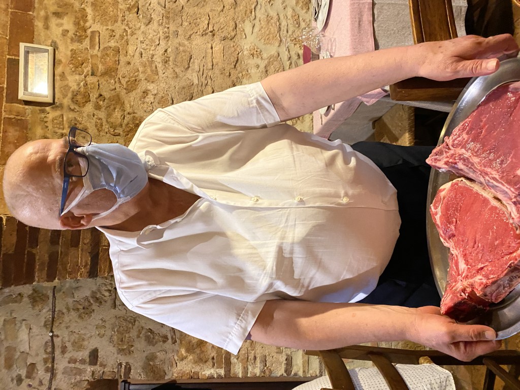 Waiter at Taverna del Vecchio Borgo presenting raw Florentine T-bone steaks on a tray