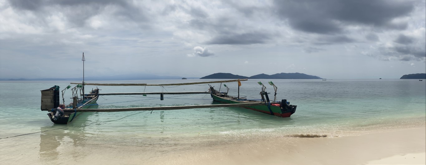 Traditional longtail fishing boats moored on a Raja Ampat sandy shore, islands visible in the distance