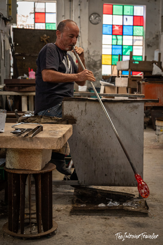 Murano glassblower shaping molten red glass on a blowpipe in a traditional island furnace workshop