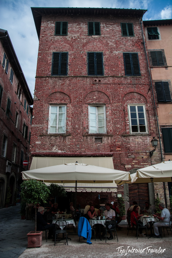 Outdoor cafe dining at Mama Butterfly restaurant beside a historic red brick building in Lucca, Tuscany