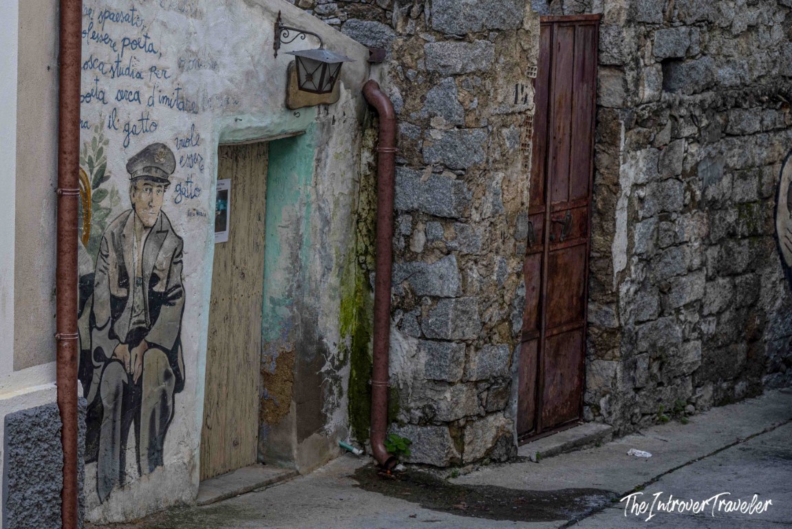 Street mural of a uniformed figure with Italian poetry text on a stone wall in Orgosolo, Sardinia