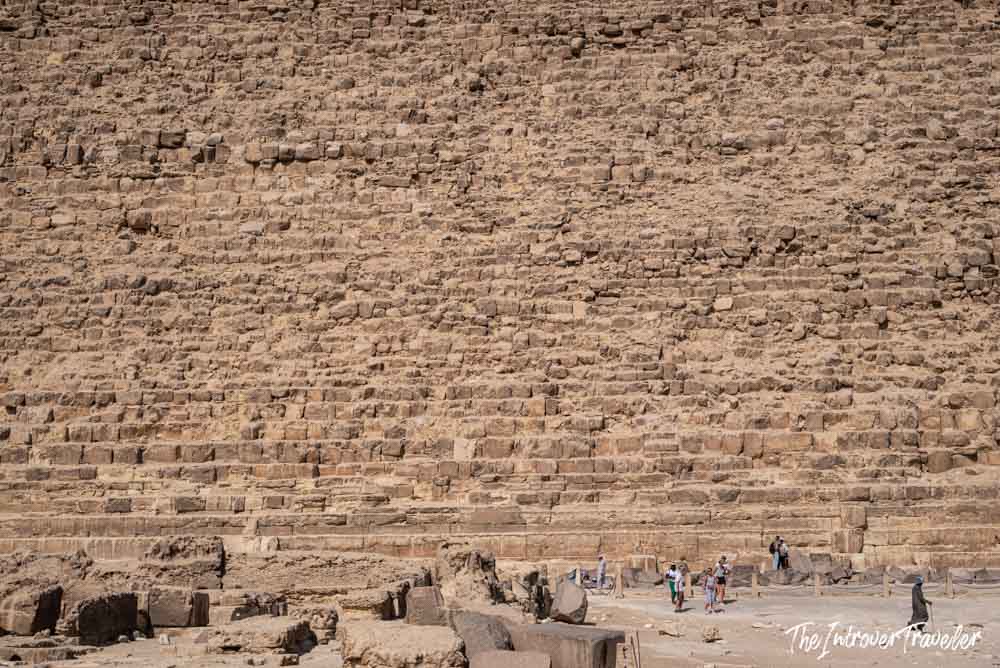 Tourists dwarfed by the massive limestone base blocks of the Great Pyramid of Giza, Egypt
