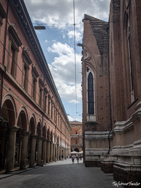 Narrow Bologna street flanked by the Archiginnasio Palace porticoes and the flank of San Petronio Basilica