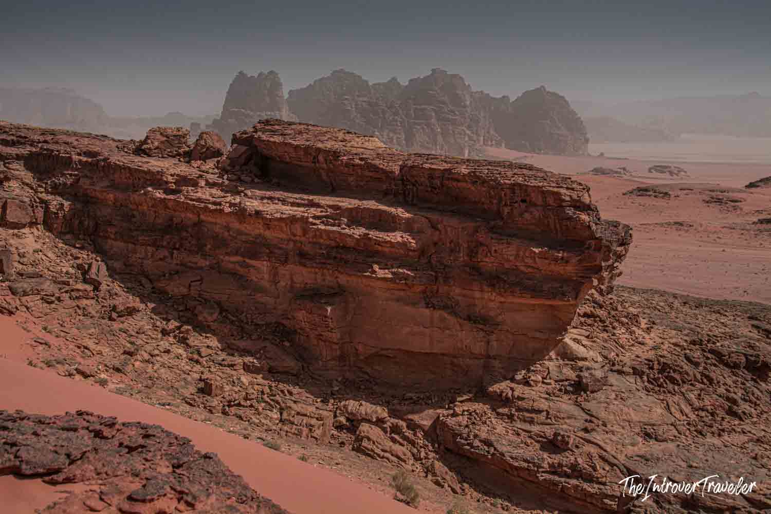 Layered red sandstone rock formation in Wadi Rum desert, Jordan, with hazy mountains in the background