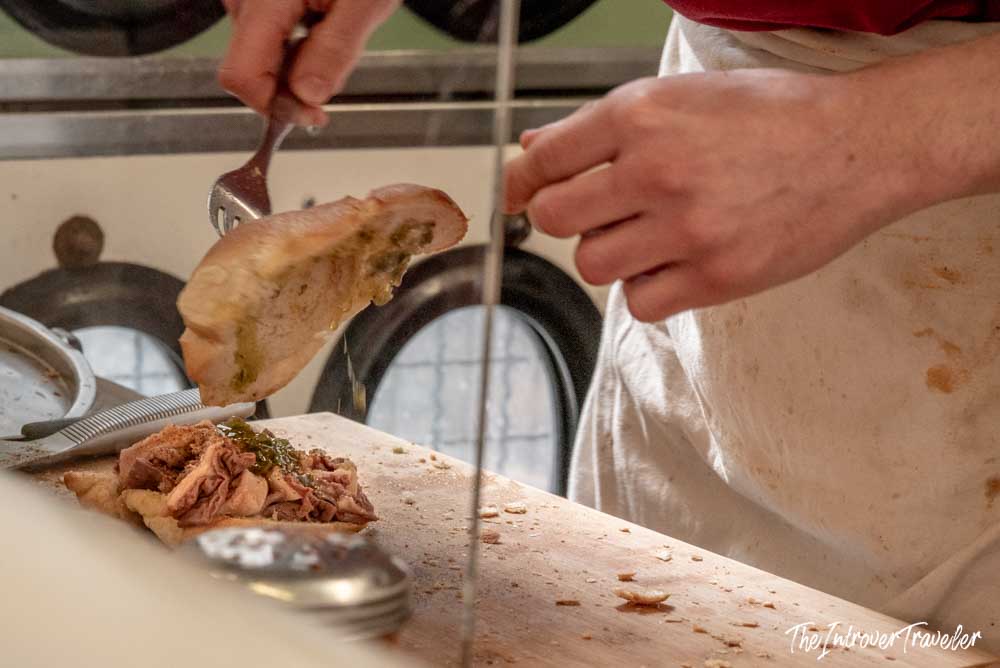 Vendor assembling a lampredotto sandwich with salsa verde on a wooden cutting board in Florence