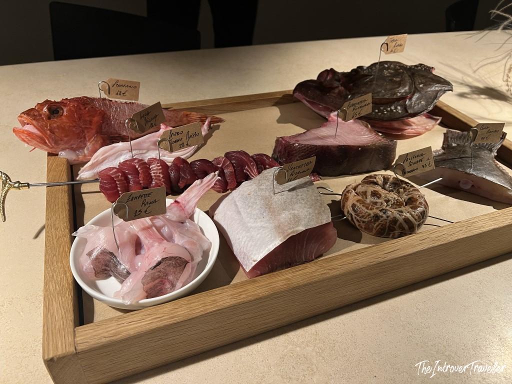 Raw seafood selection on a wooden tray at Trattoria Da Lucio, Rimini, with handwritten price tags