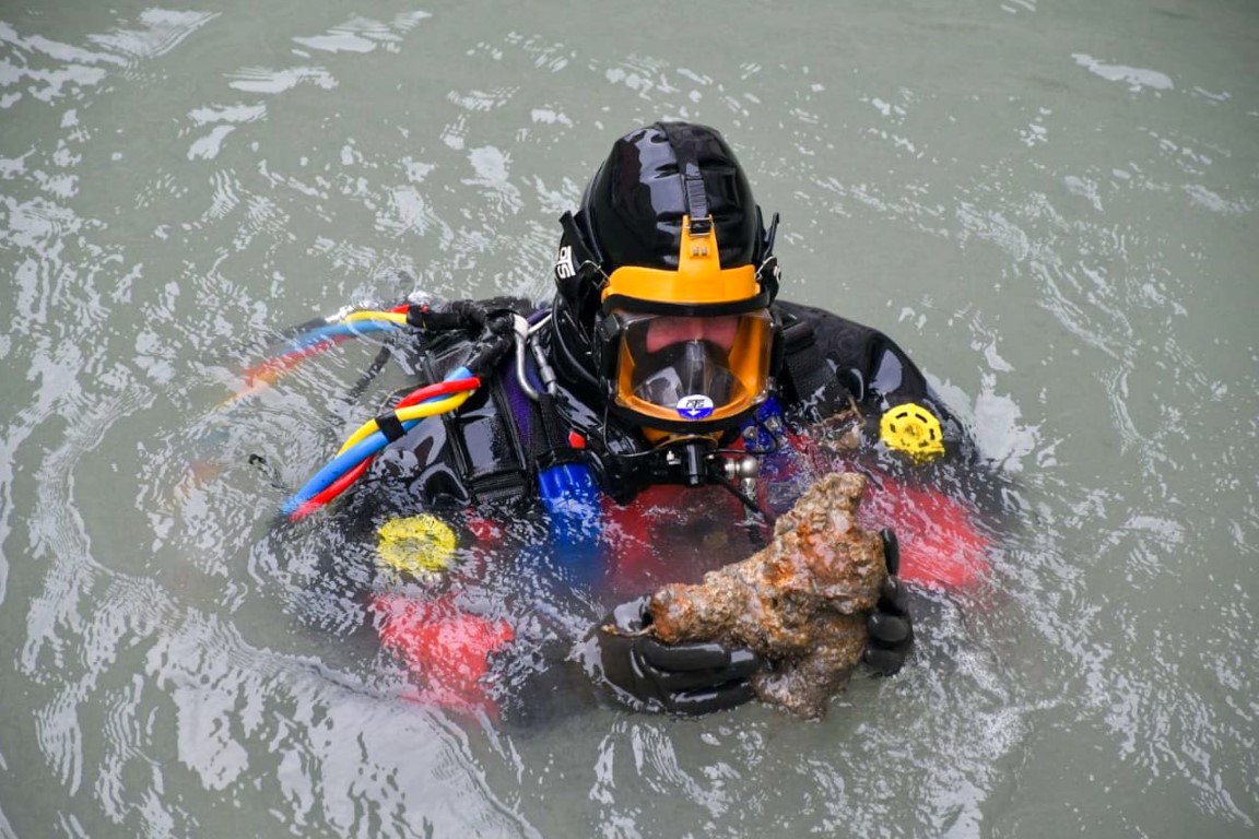 Diver surfacing in a Venice canal holding an encrusted artifact recovered from the murky waterway