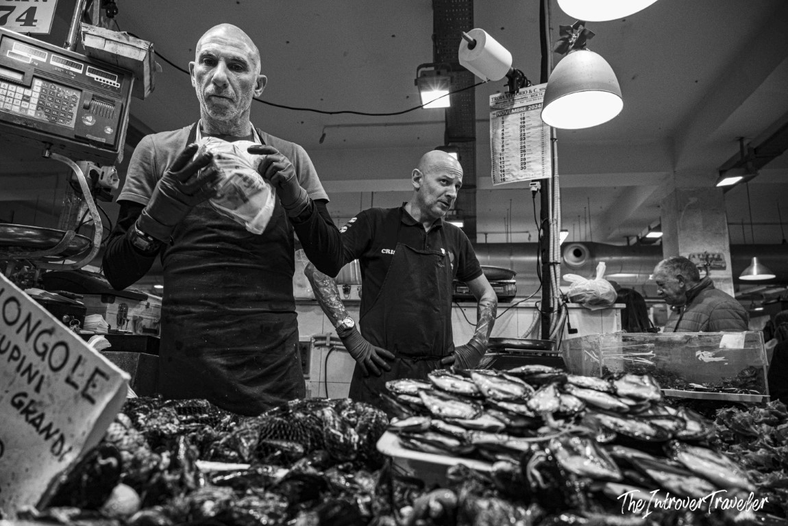 Two fishmongers working a busy Italian fish market stall, with vongole and fresh catch on display