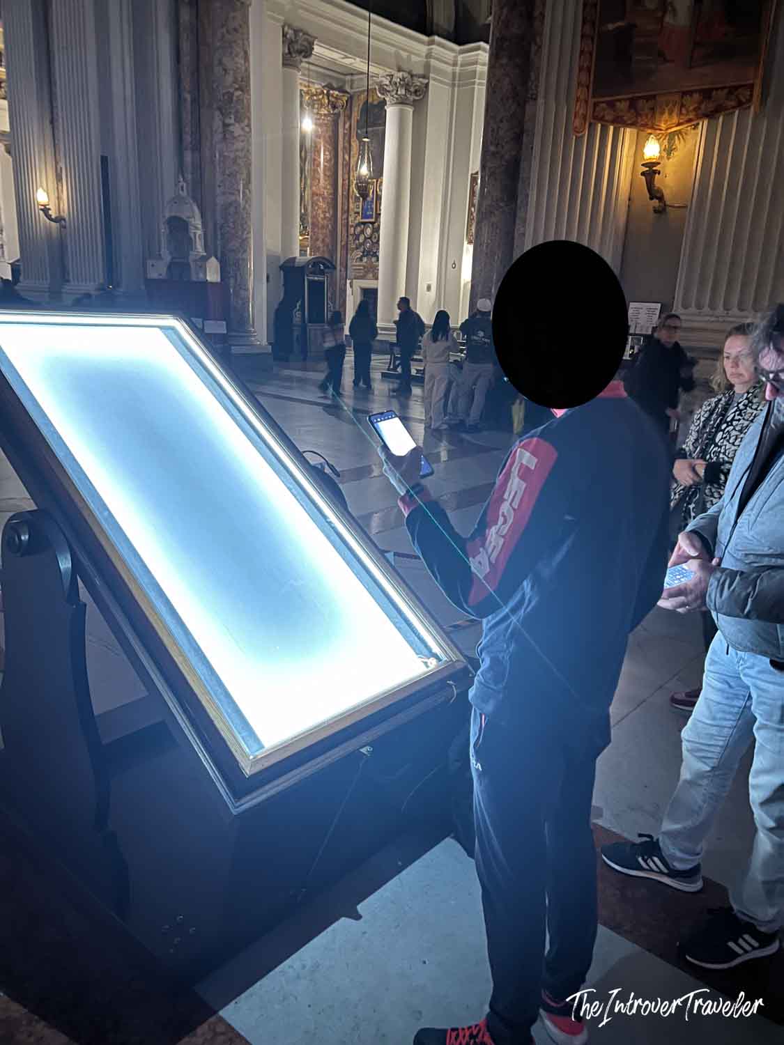 Visitors examining a backlit display panel inside Sant'Ignazio church, Rome, with ornate columns behind