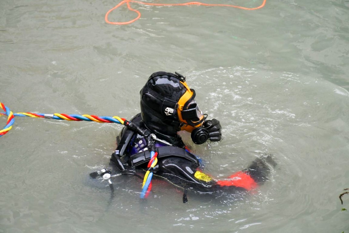 Professional venice canal diver in black dry suit and yellow helmet, tethered with safety lines