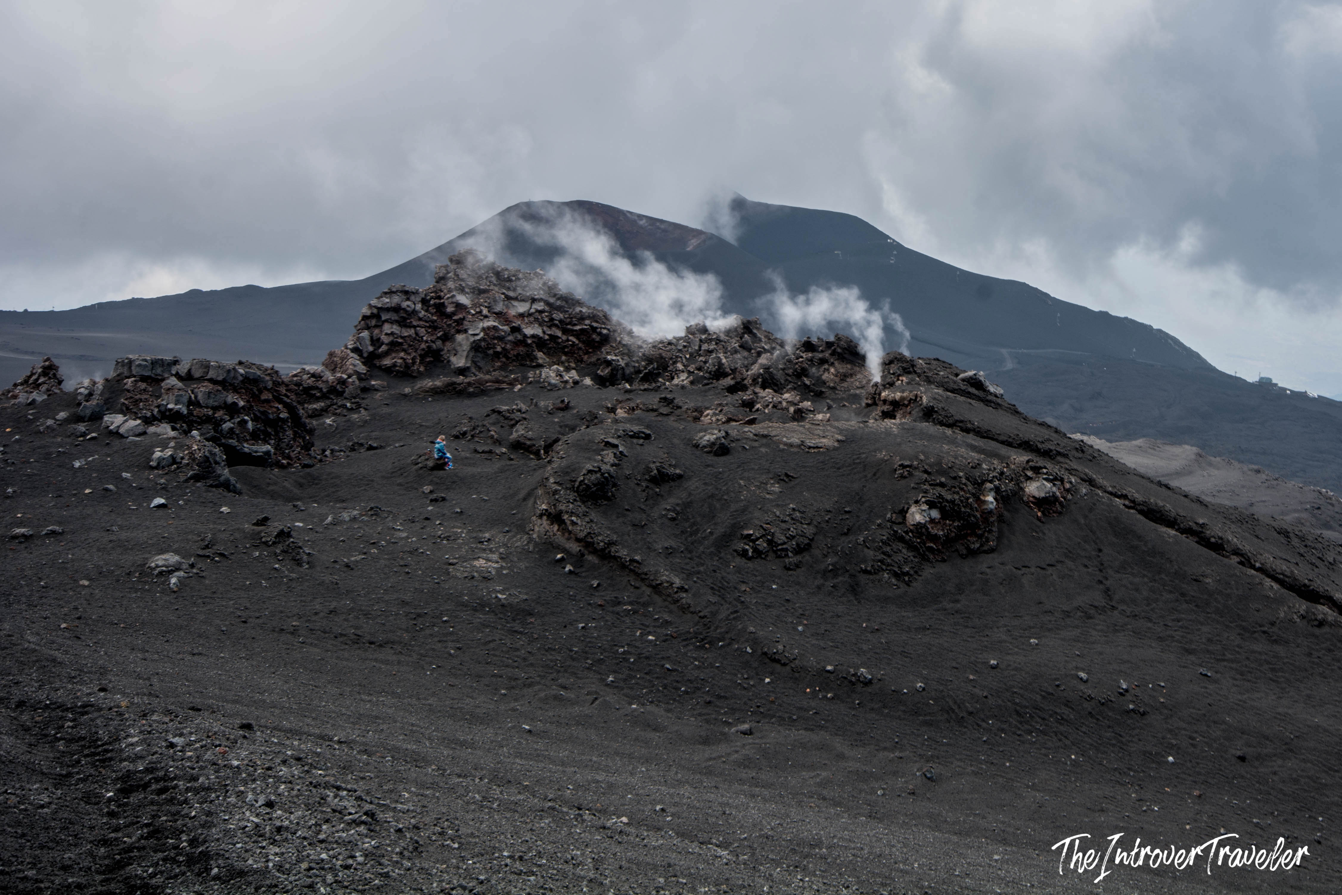 Hiker dwarfed by Mount Etna's black lava fields and steaming fumaroles near the summit craters