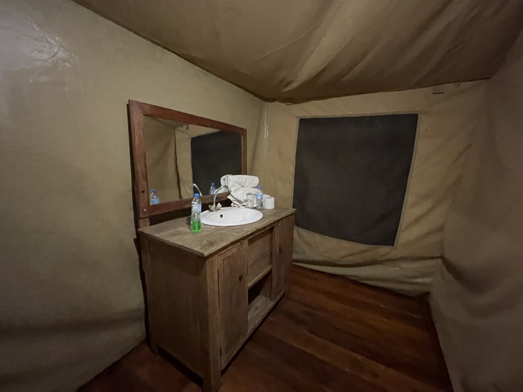 Safari tent bathroom in Tanzania with wooden vanity, sink, mirror, and towels inside canvas walls