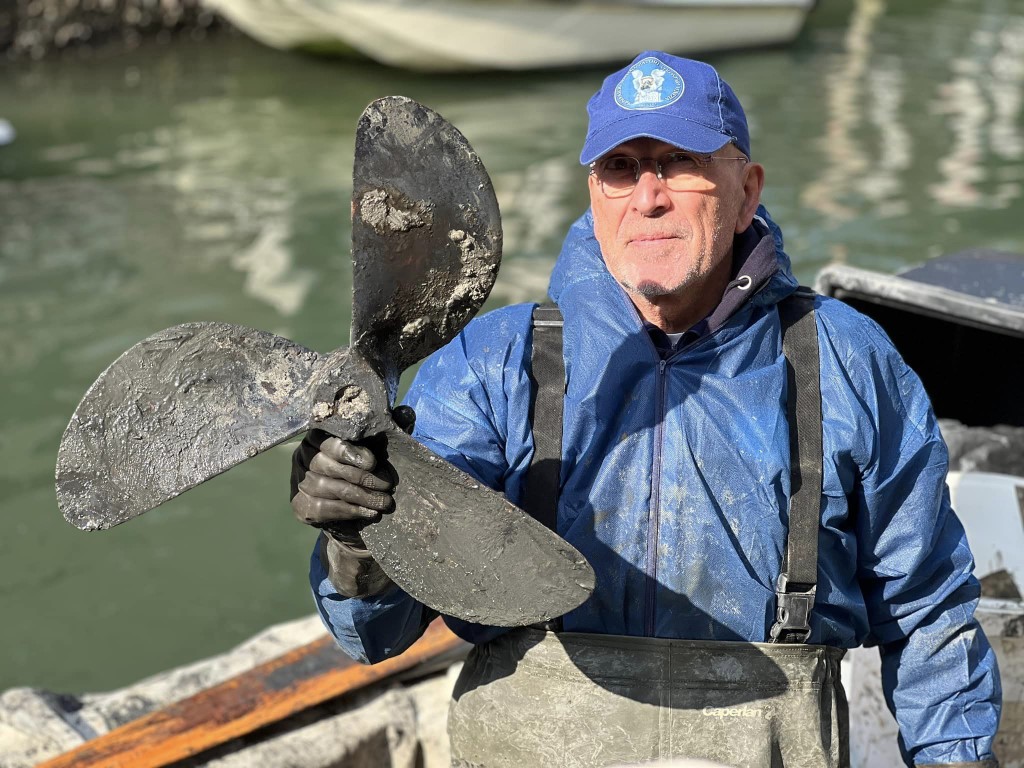 Volunteer canal diver in Venice holding a recovered encrusted boat propeller from the lagoon