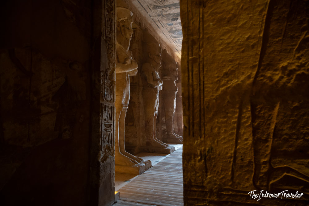 Dimly lit hypostyle hall inside Abu Simbel temple, with Osirid pillar statues of Ramesses II lining the corridor