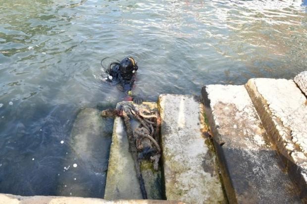 Scuba diver surfacing near weathered stone steps in a Venice canal with tangled rope debris