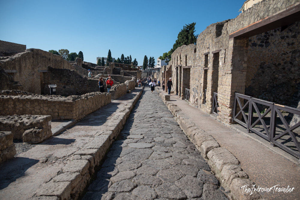 Ancient cobblestone street at Herculaneum excavations with visitors walking past preserved Roman ruins