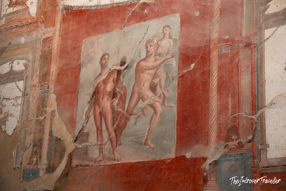 Ancient Roman fresco with mythological figures on a cracked red wall at Herculaneum excavations