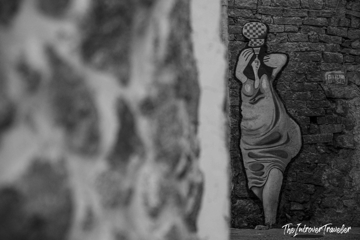 Street mural in Orgosolo, Sardinia, showing a stylized woman balancing a checkered vessel on her head
