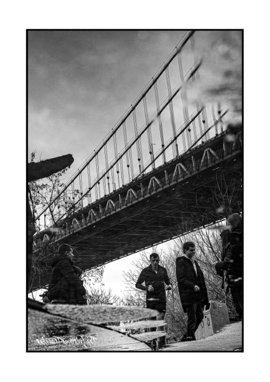 Black and white street photo of pedestrians beneath the Manhattan Bridge, New York, December 2024