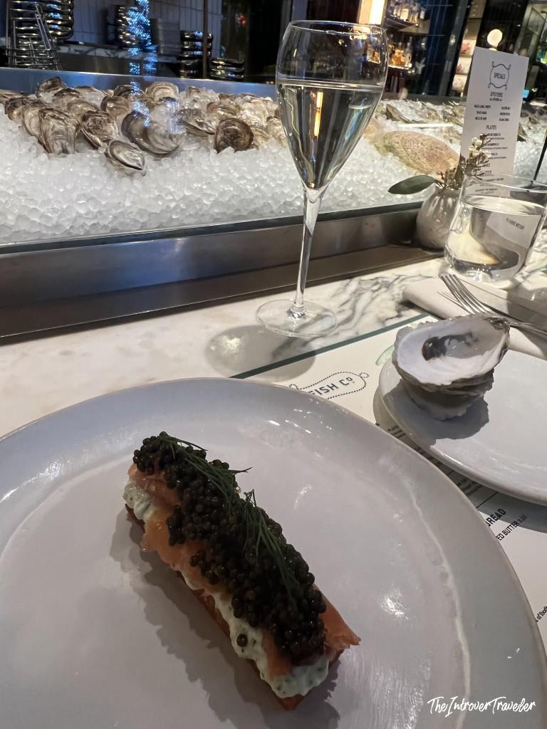 Salmon toast topped with caviar and dill at Fulton Fish Bar, with oysters on ice in the background