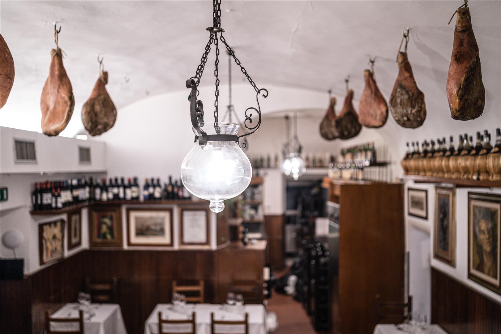 Interior of Trattoria Il Latini Florence, with cured ham legs hanging from vaulted ceiling