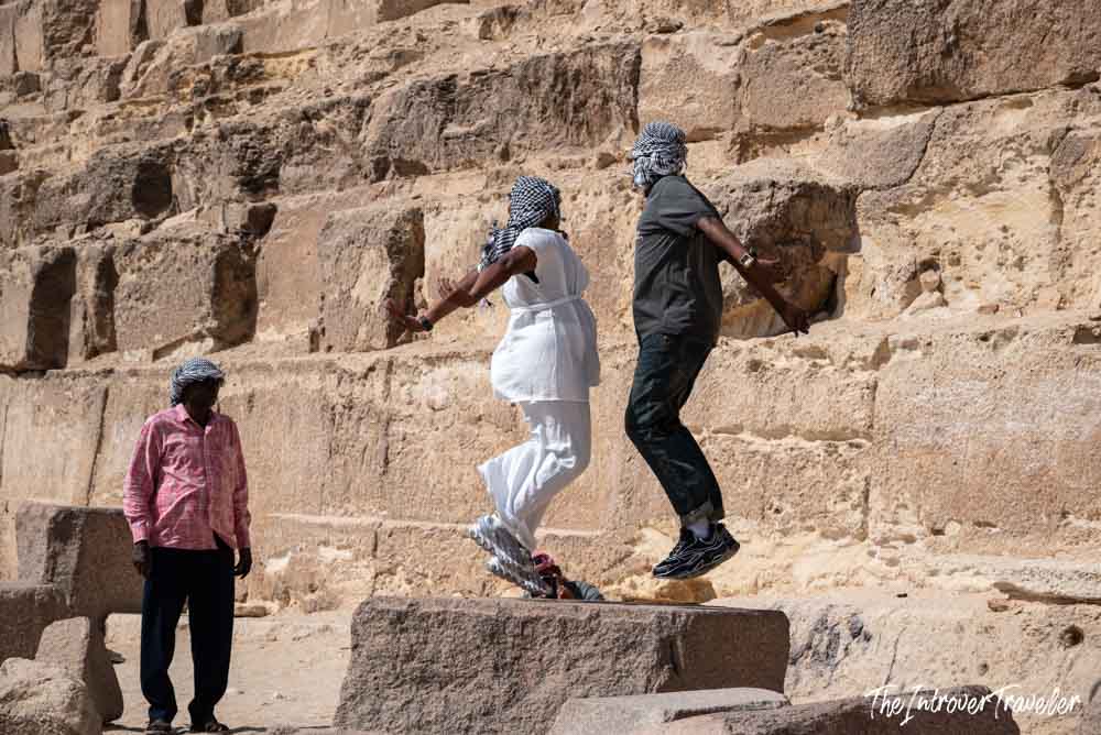 Tourists jumping for photos on the ancient limestone blocks at the base of the Pyramids of Giza