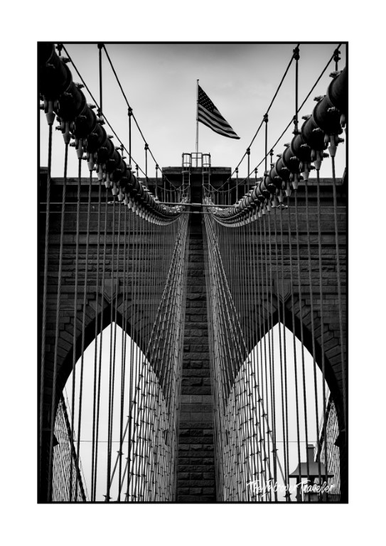Black and white close-up of Brooklyn Bridge tower, cables, and American flag, New York