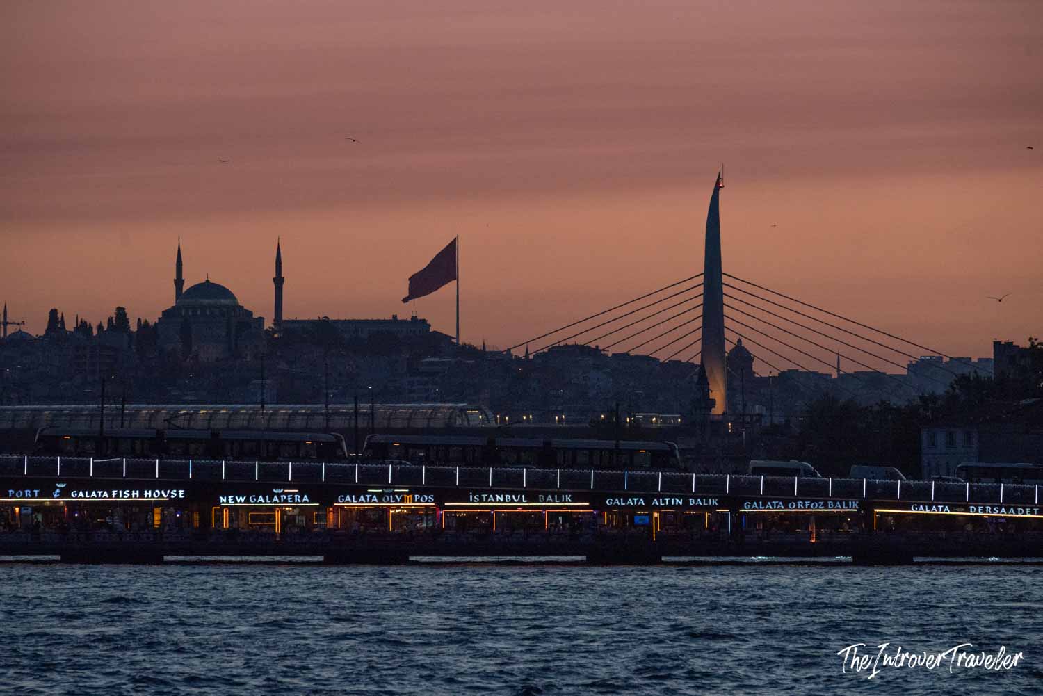Galata Bridge fish restaurants at dusk, with a mosque silhouette on the Istanbul skyline