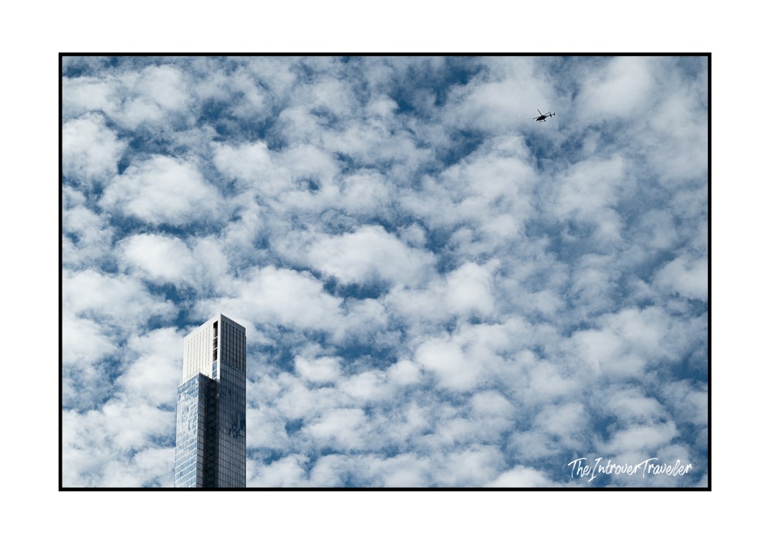 Glass skyscraper top against a cloudy New York sky, with a helicopter flying overhead