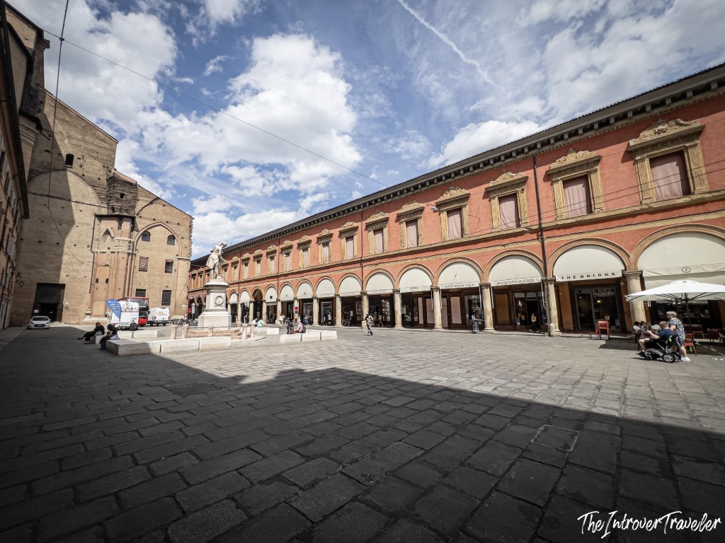 Piazza Galvani in Bologna with the Archiginnasio arcade and a central monument under blue skies