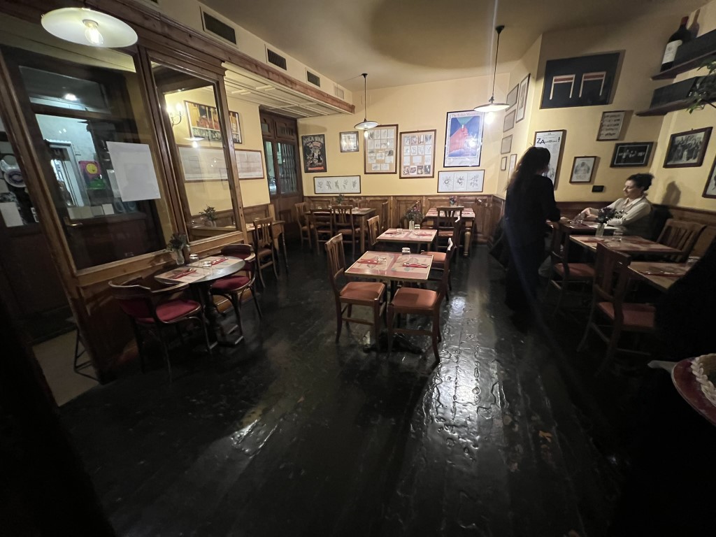 Cozy dining room at Trattoria Cibrèo Florence, with wooden chairs, set tables, and vintage posters on warm yellow walls.
