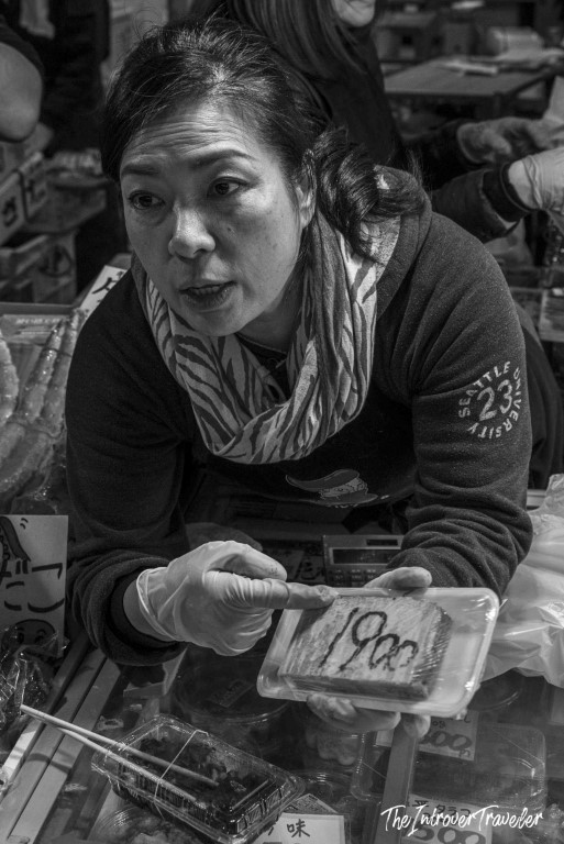 Tsukiji market vendor in gloves showing packaged seafood priced at 1900 yen, Tokyo