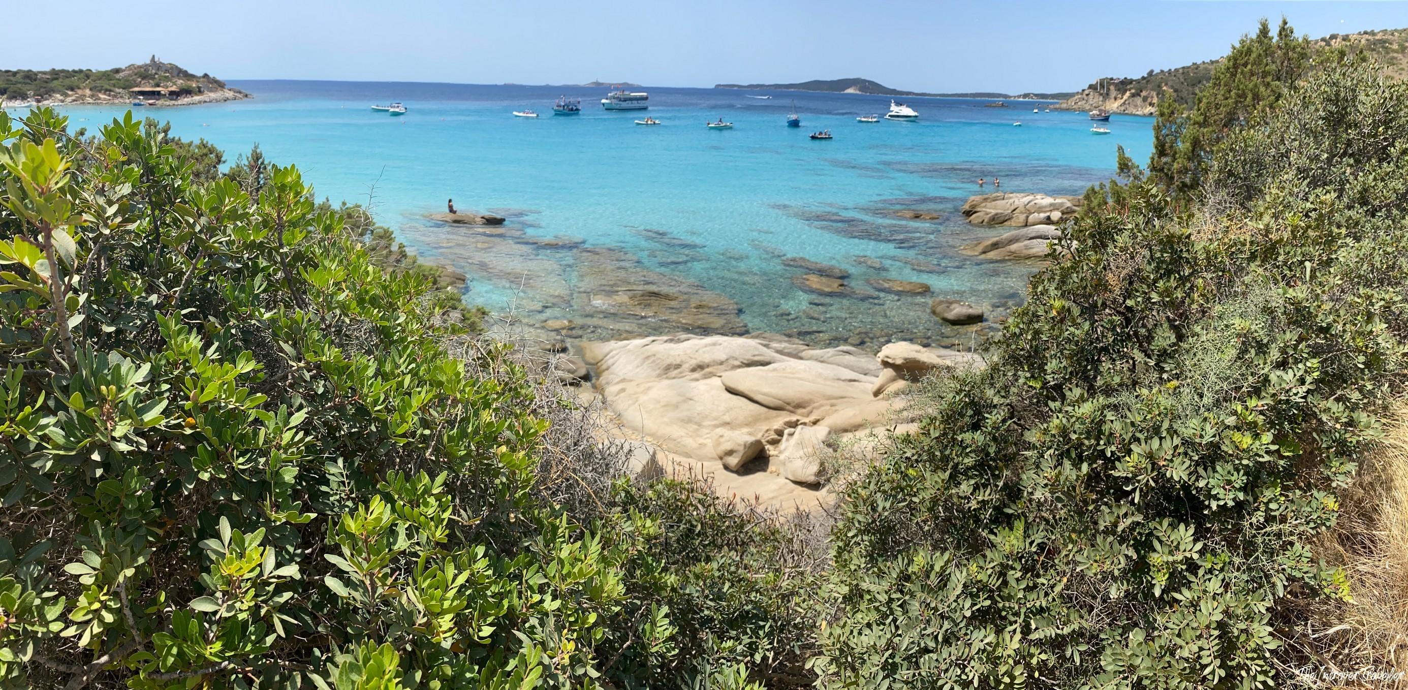 Turquoise cove in south Sardinia, with granite rocks, Mediterranean scrub, and boats anchored offshore