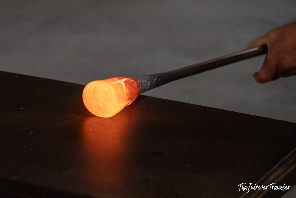 Murano glassblower shaping glowing molten glass on a blowpipe at a Venice furnace