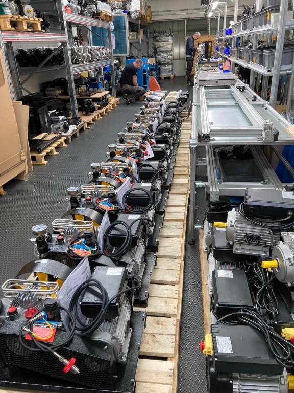Compressor units lined up on a factory floor, assembled by technicians in an industrial workshop