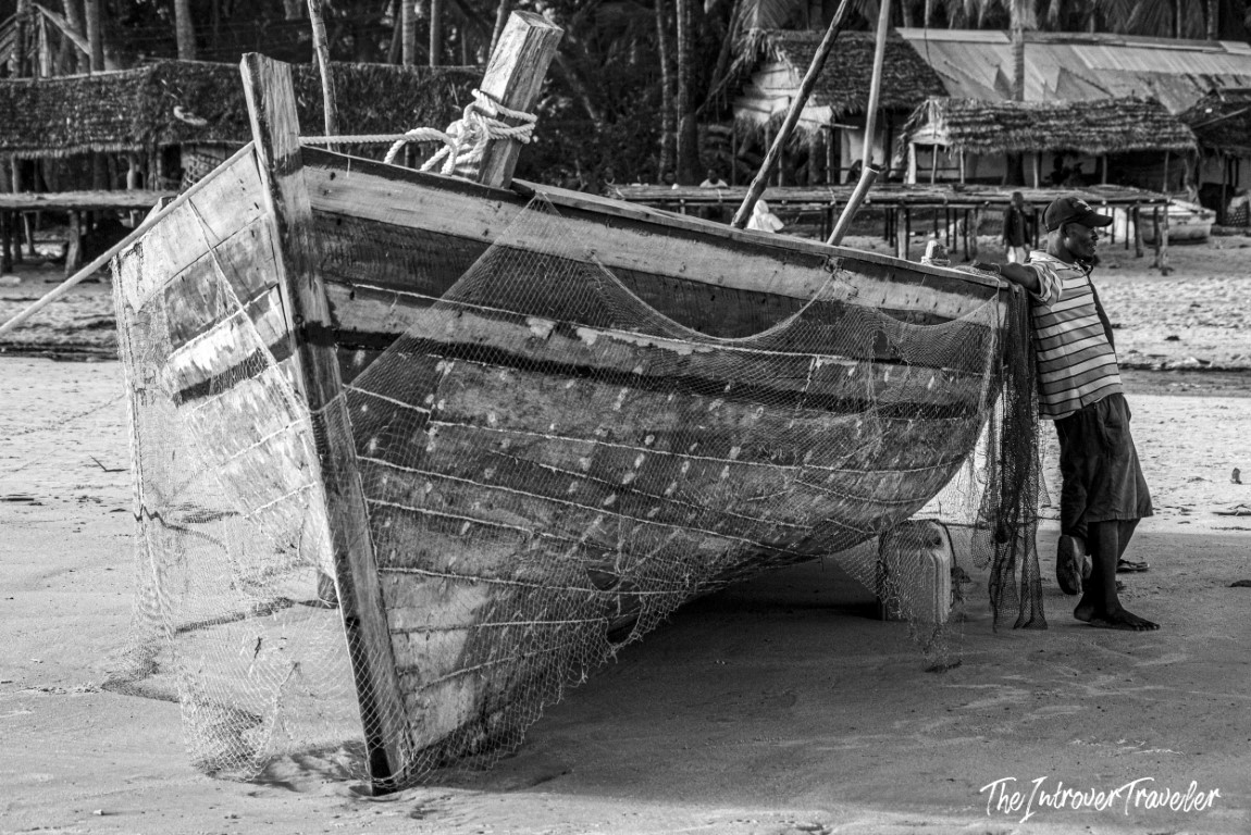 Fisherman tending nets beside a weathered wooden boat on a sandy coastal beach village