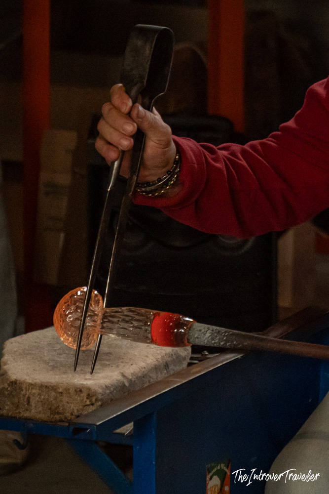 Murano glassmaker shaping molten glass with iron tongs and blowpipe at a Venice furnace