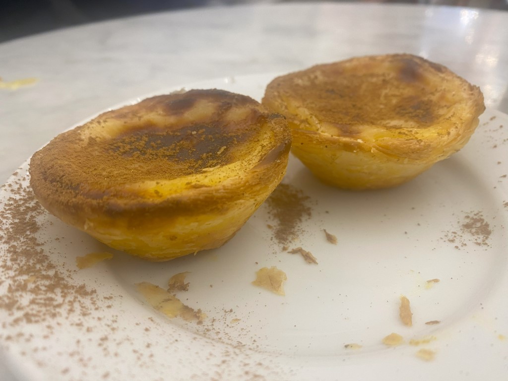 Two freshly baked pasteis de nata from Porto, dusted with cinnamon on a white plate