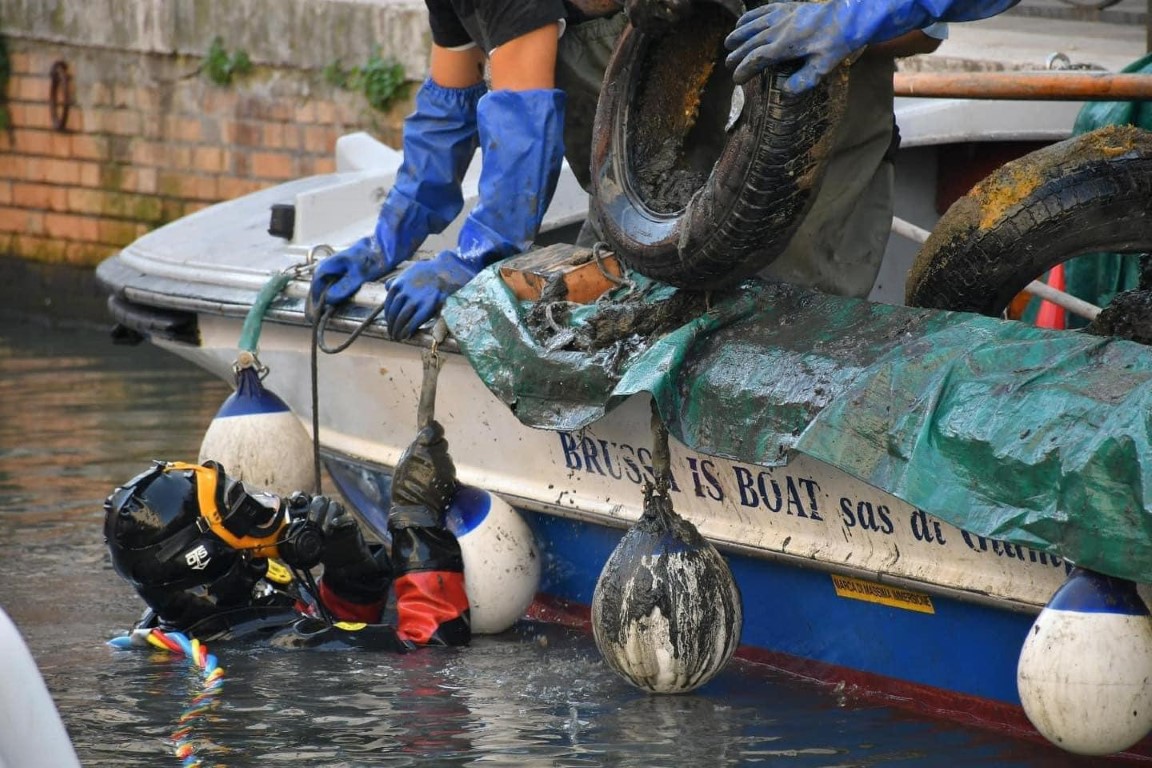 Diver and crew removing tires and debris from a Venice canal beside a cleanup boat