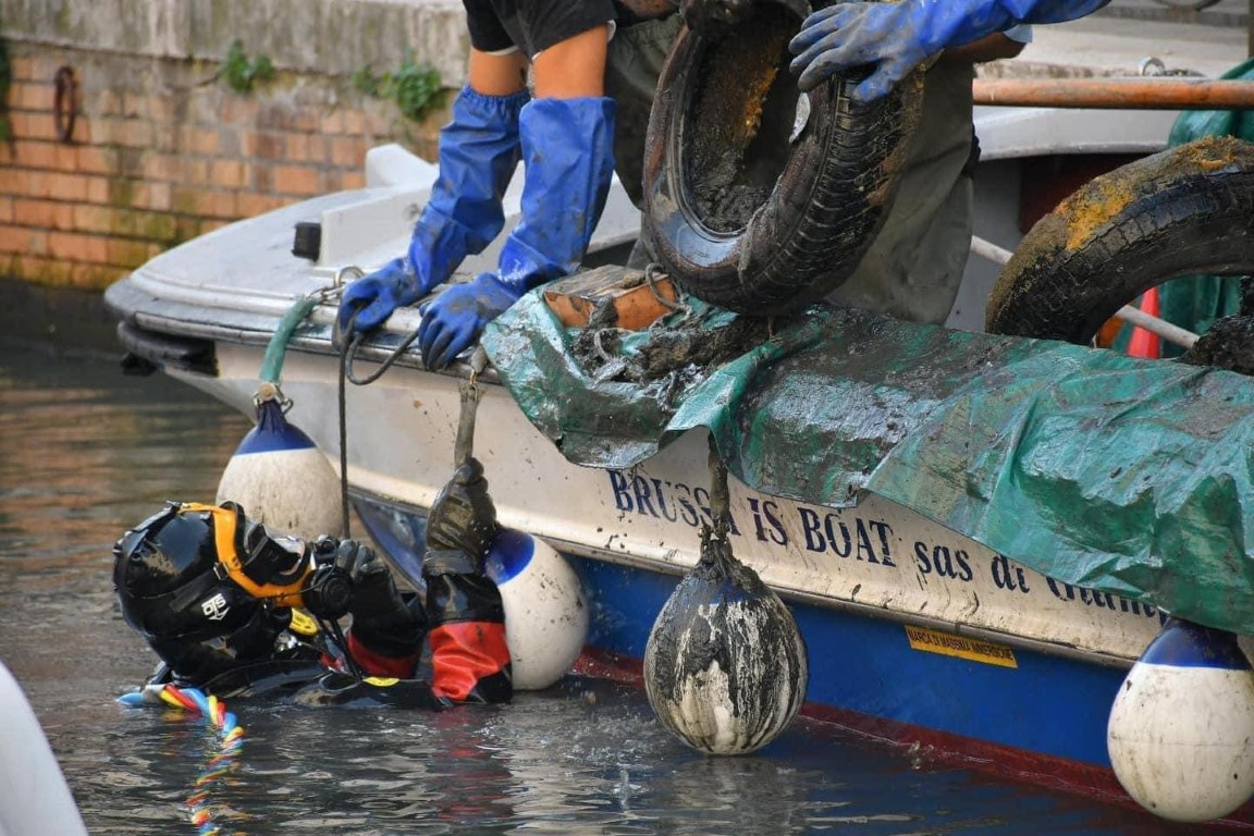 Volunteer diver and crew hauling mud-covered tires from a Venice canal during a cleanup dive