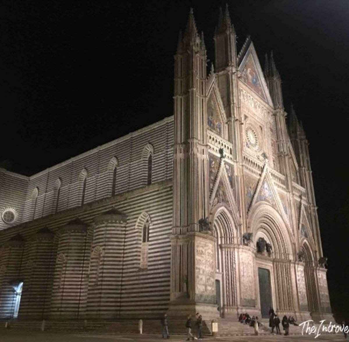 Orvieto Cathedral illuminated at night, Gothic facade with striped marble walls glowing against dark sky
